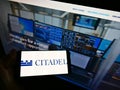 Person holding smartphone with business logo of American investment company Citadel LLC on screen in front of web page.