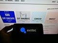 Person holding smartphone with business logo of German biotechnology company Evotec AG on display in front of website.