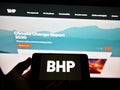 Person holding smartphone with business logo of mining, metals and petroleum company BHP Group on screen in front of webpage.