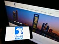 Person holding smartphone with logo of Abu Dhabi National Oil Company (ADNOC) on screen in front of website.