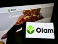 Person holding smartphone with logo of agribusiness company Olam International Limited on screen in front of website.