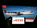 Person holding smartphone with logo of aircraft manufacturer Avions de Transport RÃÂ©gional (ATR) on screen with website.