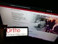 Person holding smartphone with logo of American company Ortho Clinical Diagnostics on screen in front of website.