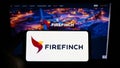 Person holding smartphone with logo of Australian gold mining company Firefinch Limited on screen in front of website.