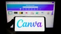 Person holding smartphone with logo of Australian graphic design company Canva Pty Ltd on screen in front of website.