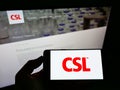 Person holding smartphone with logo of Australian pharmaceuticals company CSL Limited on screen in front of website.