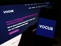 Person holding smartphone with logo of Australian telecommunications provider Vocus Group on screen in front of website.