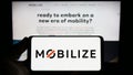 Person holding smartphone with logo of automotive mobility company Mobilize on screen in front of website.