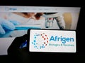 Person holding smartphone with logo of biotechnology company Afrigen Biologics Pty. Ltd. on screen in front of website.