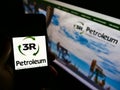 Person holding smartphone with logo of Brazilian oil and gas company 3R Petroleum S.A. on screen in front of website.