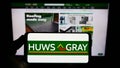 Person holding smartphone with logo of British builders merchant company Huws Gray Limited on screen in front of website.