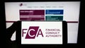 Person holding smartphone with logo of British Financial Conduct Authority (FCA) on screen in front of website. Royalty Free Stock Photo