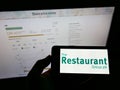 Person holding smartphone with logo of British gastronomy company The Restaurant Group plc on screen in front of website.