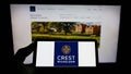 Person holding smartphone with logo of British housebuilding company Crest Nicholson plc on screen in front of website.