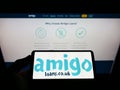 Person holding smartphone with logo of British loan guarantor Amigo Holdings PLC on screen in front of website.