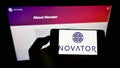 Person holding smartphone with logo of British private equity firm Novator Partners LLP on screen in front of website.