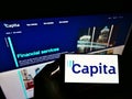 Person holding smartphone with logo of British process outsourcing company Capita plc on screen in front of website. Royalty Free Stock Photo