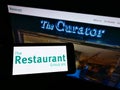Person holding smartphone with logo of British pub company The Restaurant Group plc on screen in front of business website.