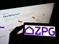 Person holding smartphone with logo of British real estate company ZPG Limited on screen in front of website.