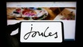 Person holding smartphone with logo of British retail company Joules Group plc on screen in front of website.