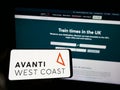 Person holding smartphone with logo of British train company Avanti West Coast on screen in front of website.