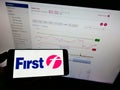 Person holding smartphone with logo of British transport company FirstGroup plc on screen in front of website.