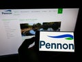 Person holding smartphone with logo of British water utility company Pennon Group plc on screen in front of website.