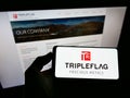 Person holding smartphone with logo of Canadian company Triple Flag Precious Metals Corp. on screen in front of website.