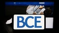 Person holding smartphone with logo of Canadian telecommunications company BCE Inc. on screen in front of website.