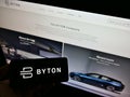 Person holding smartphone with logo of Chinese automotive brand Byton (electric vehicle) on screen in front of website.