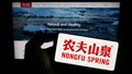 Person holding smartphone with logo of Chinese business Nongfu Spring Company Limited on screen in front of website.