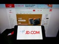 Person holding smartphone with logo of Chinese e-commerce company JD.com Inc. on screen in front of website.