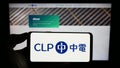 Person holding smartphone with logo of Chinese energy company CLP Group on screen in front of website.