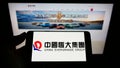Person holding smartphone with logo of Chinese property company Evergrande Real Estate Group on screen in front of website.