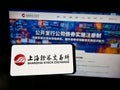 Person holding smartphone with logo of Chinese Shanghai Stock Exchange (SSE) on screen in front of website.