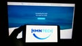 Person holding smartphone with logo of Chinese submarine network company HMN Tech on screen in front of website.