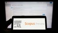 Person holding smartphone with logo of citation database Scopus Preview on screen in front of website.