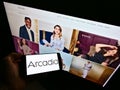 Person holding smartphone with logo of clothing retailing company Arcadia Group Ltd. on screen in front of web page.