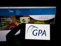 Person holding smartphone with logo of company Companhia Brasileira de DistribuiÃÂ§ÃÂ£o (GPA) on screen with website.