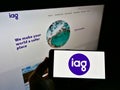 Person holding smartphone with logo of company Insurance Australia Group Limited (IAG) on screen in front of website.
