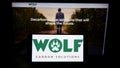 Person holding smartphone with logo of company Wolf Carbon Solutions on screen in front of website.