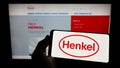 Person holding smartphone with logo of consumer goods company Henkel AG Co. KGaA on screen in front of website. Royalty Free Stock Photo