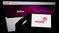 Person holding smartphone with logo of consumer goods company Reckitt Benckiser Group plc on screen in front of web page.