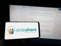 Person holding smartphone with logo of content hosting company SlideShare on screen in front of website.