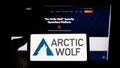 Person holding smartphone with logo of cybersecurity company Arctic Wolf Networks Inc. on screen in front of website.