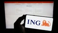 Person holding smartphone with logo of Dutch financial services company ING Groep N.V. on screen in front of website.