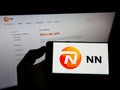 Person holding smartphone with logo of Dutch insurance company NN Group N.V. on screen in front of website.