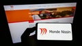 Person holding smartphone with logo of Filipino food company Monde Nissin Corporation on screen in front of website.