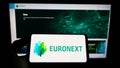 Person holding smartphone with logo of financial services company Euronext N.V. on screen in front of website.