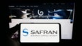 Person holding smartphone with logo of French aerospace company Safran S.A. on screen in front of website. Royalty Free Stock Photo